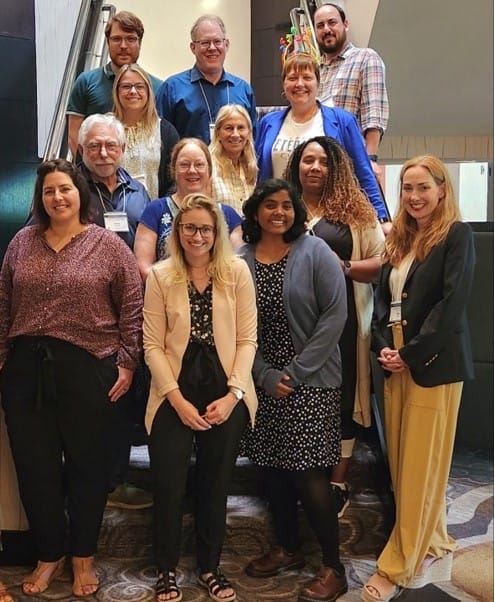 A group of about sixteen people poses together for a photo indoors.